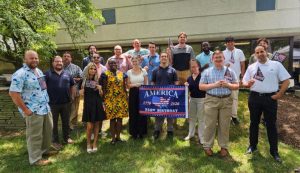 Group of diverse adults posing outdoors, holding a banner celebrating America’s 250th birthday (1776–2026).