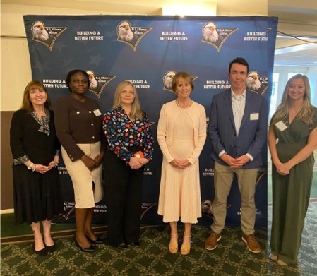 Seven professionals posing for a group photo at a 'Building a Better Future' event, in front of a blue branded backdrop with logos.