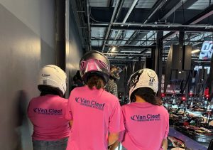 People in pink Van Cleef shirts with helmets, seen from behind, in a motorcycle showroom.