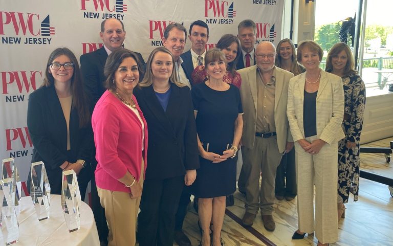 Group of business professionals posing for a photo at a PWC New Jersey event, in front of a branded backdrop.
