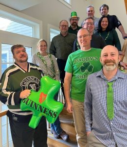 Group of coworkers on a staircase wearing green for a St. Patrick's Day celebration, with a large green Guinness balloon in the foreground.