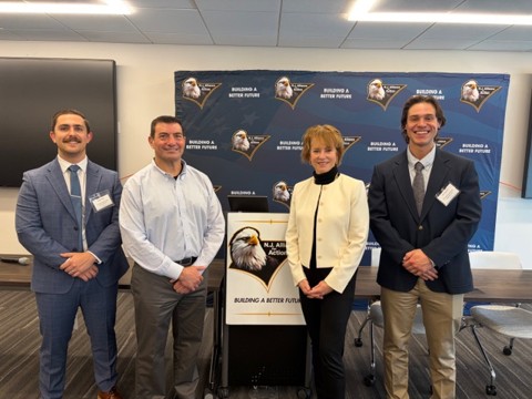 Four professionals in business attire pose for a photo at a conference, with a 'Building a Better Future' banner behind them and a podium in front of the group.