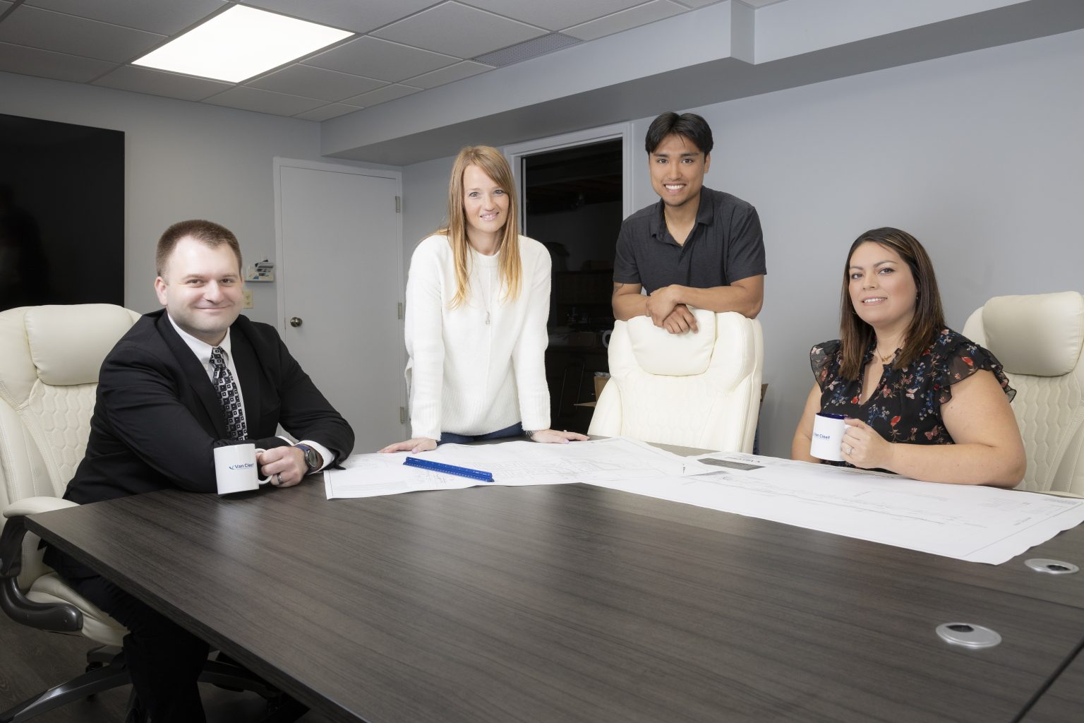 Four professionals sit around a conference table with papers and mugs in a modern office meeting room.