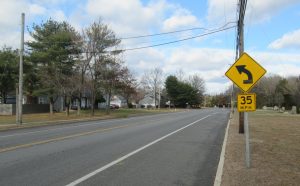 Suburban street with utility poles and a yellow warning sign for a left-curving road, plus a 35 mph speed limit sign.